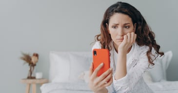 Caucasian woman sat on bed doomscrolling on mobile phone